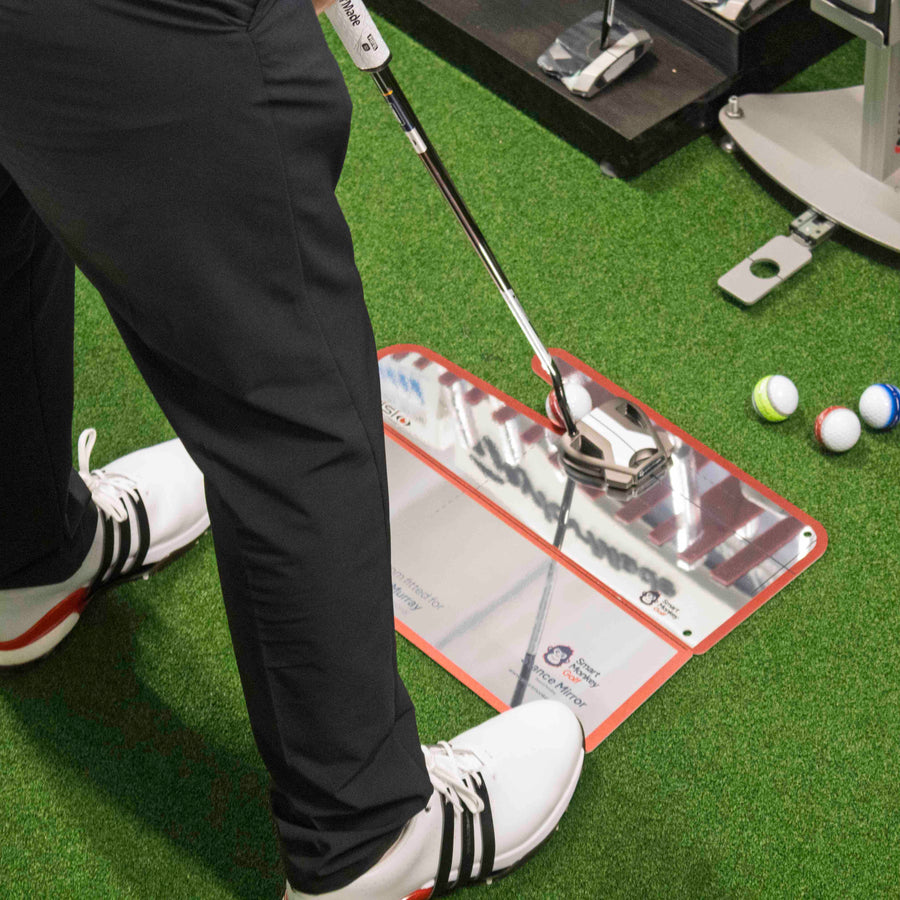 Club Stance Mirror in use indoors, reflecting the golfer's putter head and shaft angle at address